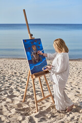 Young woman artist paints vibrant portrait on beach, surrounded by tranquil sea and sky. Her focus...