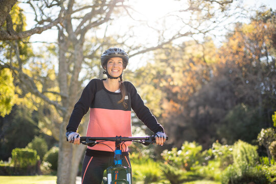 Woman wearing cycling helmet and gloves holding bicycle handlebars while riding through public park
