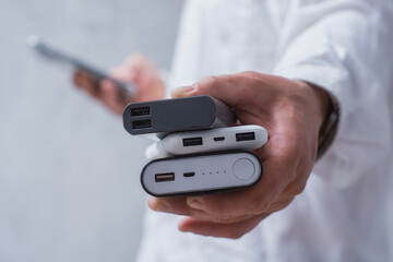 Man hand holds three different power bank. Modern portable chargers with USB connectors for charging smartphones and gadgets.