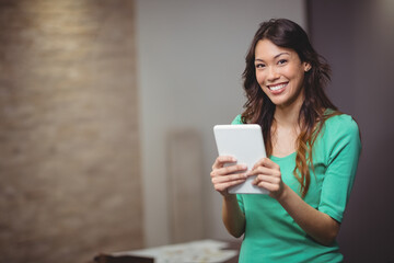 Asian woman smiling and holding white tablet at home office with documents on table, copy space