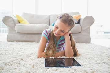 Girl lying on white shag carpet in front of gray sofa with colorful pillows using tablet