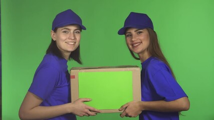 Two cheerful female delivery service workers smiling while holding a cardboard box