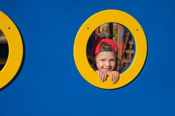 Funny girl peeks through a hole in the playground