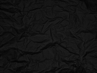 Crinkled black textured surface with folds and creases creating an abstract pattern. No text present. Dark and moody atmosphere with irregular shapes and shadows on the material