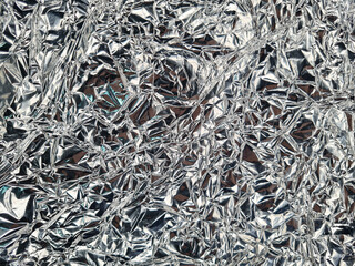 Crinkled silver metallic surface, creating an abstract texture with intricate folds and reflections. The shiny wrinkles form a chaotic pattern, enhancing light interplay and shimmering appeal