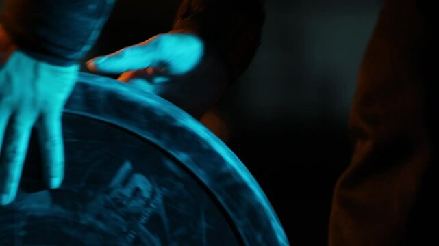 Close-up of an athlete's hands with wrist wraps grabbing a heavy weight plate. Dramatic blue and warm lighting creates a powerful, focused, and cinematic training atmosphere.