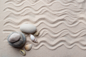 rocks and shells lie on the light sand with a pattern of waves