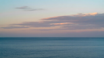 The calm ocean meets a pastel sky during a peaceful, colorful sunset.