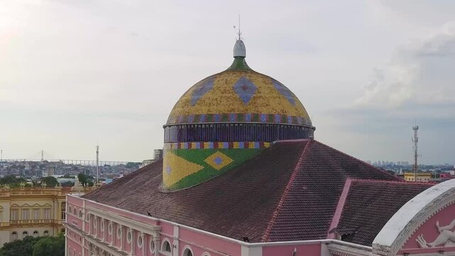 C&uacute;pula do Teatro Amazonas vista de cima, com azulejos coloridos nas cores da bandeira brasileira, destacando-se no cora&ccedil;&atilde;o de Manaus como s&iacute;mbolo da riqueza cultural.