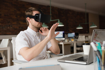 VR headset sitting beside laptop and steaming coffee cup on office desk under green pendant lamps