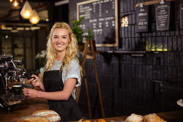 Smiling female barista using portafilter to fill coffee cup on espresso machine at shop counter