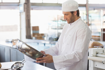 Male chef in uniform holding stainless mixing bowl while inspecting at bakery kitchen, copy space