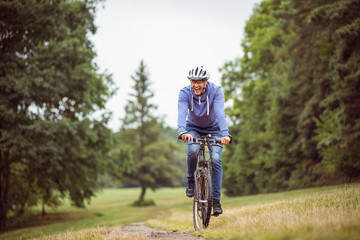 Fototapeta premium Man wearing helmet and glasses riding mountain bike along dirt trail through grassy meadow at park
