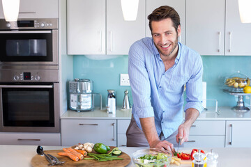 Man smiling and slicing carrots with chef's knife on wooden cutting board at kitchen island