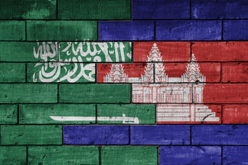 Obraz premium colourful painted big national flag of saudi arabia and flag of cambodia on a massive old brick wall background. concept