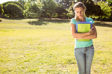 Female student standing holding colorful binders in sunny grassy park with tree shadows, copy space