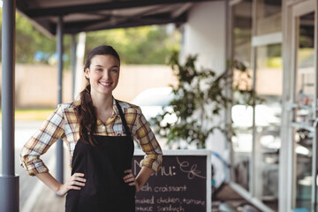 Female barista smiling while standing outside cafe under covered walkway with chalkboard menu sign