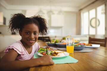 Child is eating salad, rice, chicken on mint green placemat at wood table in modern kitchen