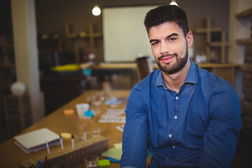 Male in his twenties sitting at table in office reviewing papers by pencil organizer, copy space