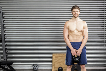 Man gripping kettlebell at thigh level in gym with weight rack, plyometric box, copy space