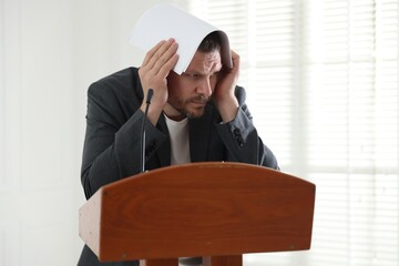 Fear of public speaking. Nervous man with microphone at lectern indoors
