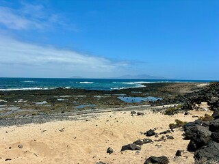 The coast of Corralejo , white sand and black volcanic rocks, Lanzarote and Isla de Lobos view in the horizon, blue sky, vacation 