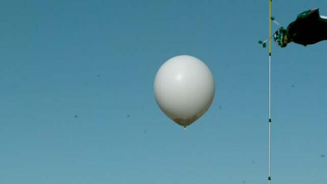 Person in wing suit soaring through air and popping large balloon with confetti - super slow motion shot