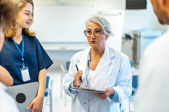 Senior doctor leading medical briefing with clipboard and pen in hospital conference room - Powered by Adobe