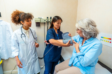 Nurse measuring blood pressure of senior woman with doctor supervising