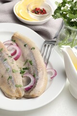 Tasty herring fillets with onions and parsley served on white table, closeup