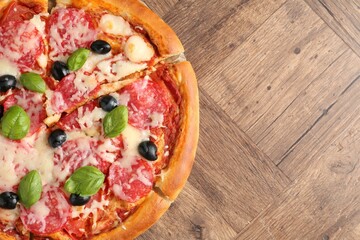 Tasty pizza with salami, cheese, basil and olives on wooden table, top view. Space for text