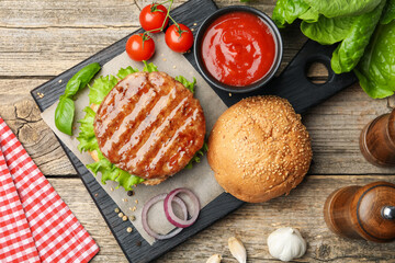 Delicious hamburger patty, bun, vegetables and spices on wooden table, flat lay