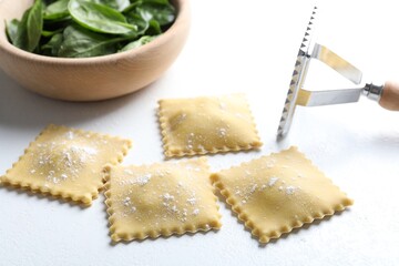 Uncooked ravioli, cutter and spinach on white table, closeup