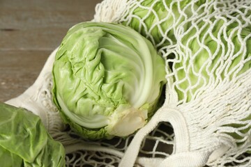 Fresh cabbages and net bag on wooden table, closeup