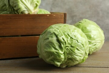 Fresh whole cabbages and crate on wooden table, closeup