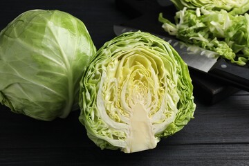 Obraz premium Fresh whole and cut cabbages on black wooden table, closeup