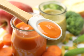 Baby food. Tasty puree in spoon, glass jars and ingredients on table, closeup