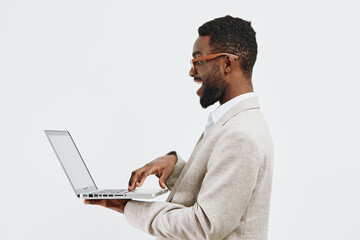 Smiling young African American man in business casual attire using laptop against plain white...