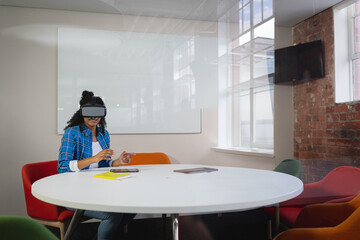 Staff wearing virtual reality headset is using yellow notebook and pen with tablet in meeting room