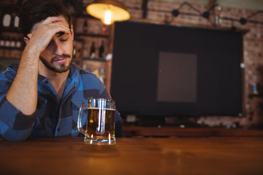 Naklejki Glass mug of beer resting on bar counter beneath glowing pendant lamp against exposed brick wall
