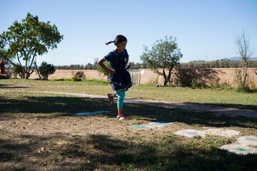 African American girl hopping over painted hopscotch squares on grass in rural park