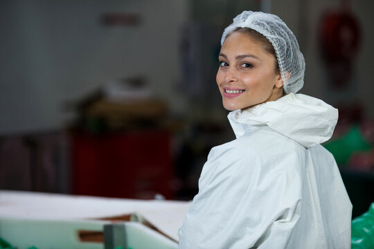 Female worker in protective suit and hairnet working at conveyor in packaging plant, copy space
