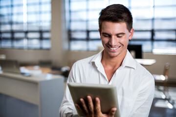 Tablet computer is being held at chest height in office by windows with blinds filtering daylight