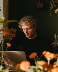 Young Man Working with Laptop Surrounded by Flowers.