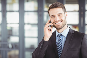 Businessman talking on smartphone in front of glass doors, with blurred office interior behind him