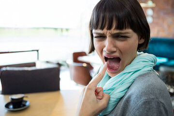 Woman in her twenties pressing finger against tongue seated at cafe table with black coffee cup