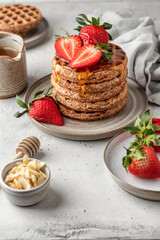 Stack of oatmeal belgian waffles with strawberry, honey and almond petals on a plate, white textured background