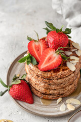 Stack of oatmeal belgian waffles with strawberry, honey and almond petals on a plate close up, white textured background