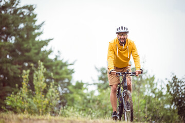 Man riding mountain bike on grassy forest trail wearing helmet and tinted sports glasses