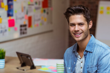 Man standing at wooden desk by whiteboard in office using tablet and sticky notes, copy space